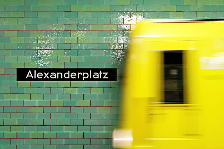  Einfahrende gelbe U-Bahn an der Station Alexanderplatz mit Schriftzug.
