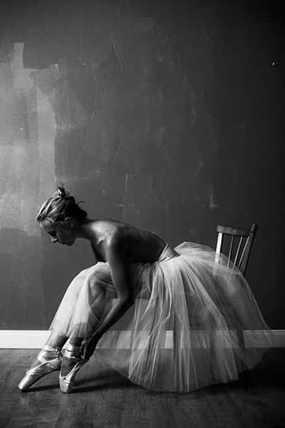 Eine Ballerina sitzt in einem Raum auf einem Stuhl und bindet sich die Schuhe