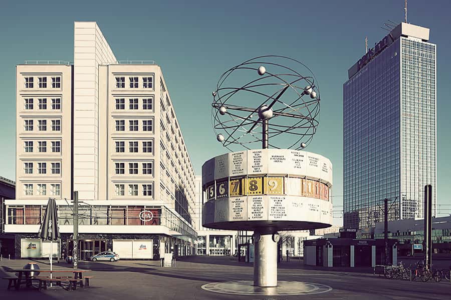 Weltzeituhr auf dem Alexanderplatz in Berlin mit Hochhaus und blauem Himmel