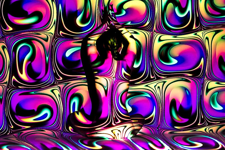 Eine Person sitzt vor einem bunten hippig beleuchteten Hintergrund