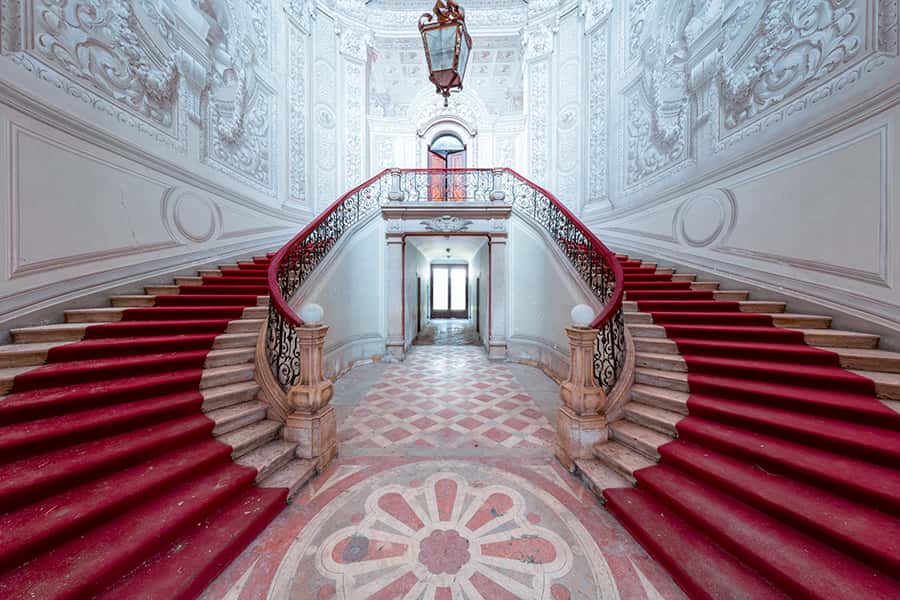 Zwei Treppen mit rotem Teppich führen den Betrachter in die zweite Etage.