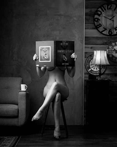 Eine nackte Frau sitzt auf einem Stuhl und liest ein Buch.
