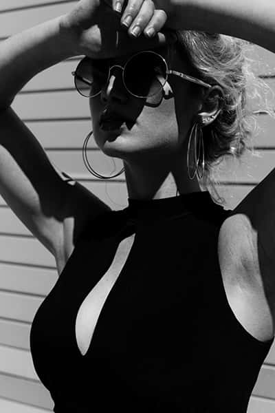 Eine Frau mit schwarzen Oberteil und Sonnenbrille blickt der Sonne entgegen