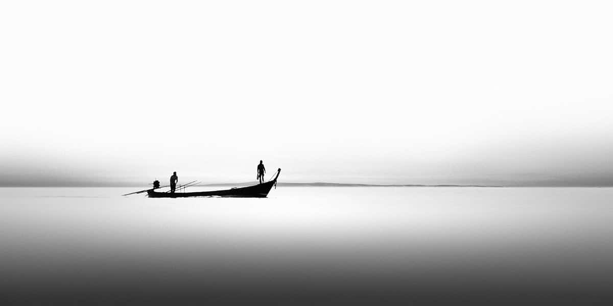 Am Horizont eines Sees sieht man ein kleines Fischerboot mit zwei Personen 