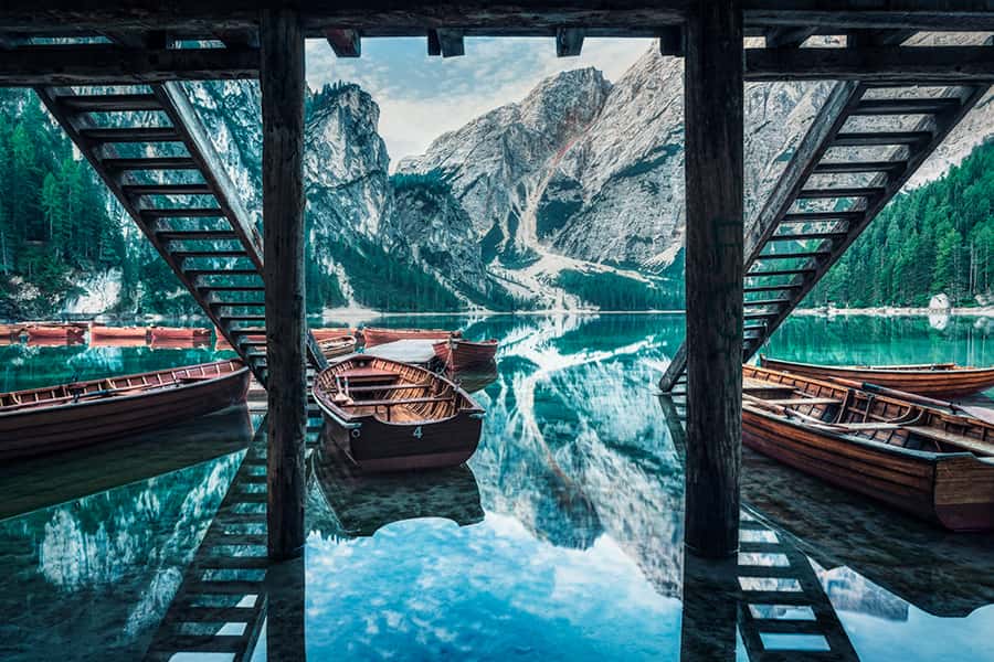Boote, Berge und eine Hütte spiegeln sich im Wasser eines Naturparkes