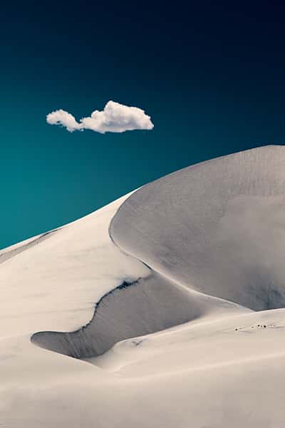 Sandfläche mit Wölbungen in weiß mit blauem Himmel wobei eine Wolke oben ist