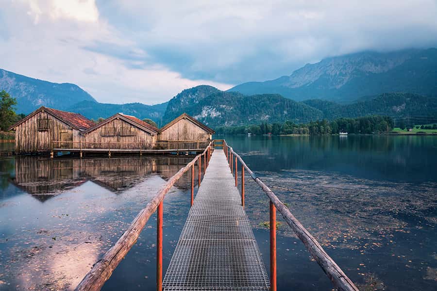 Eine Brücke führt über einen See zu drei Holzhütten